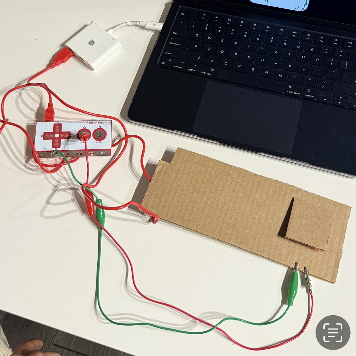 The conductive cardboard button was attached to the MakeyMakey using alligator clips. Pressing the copper-taped square completes the circuit and sends a key input.